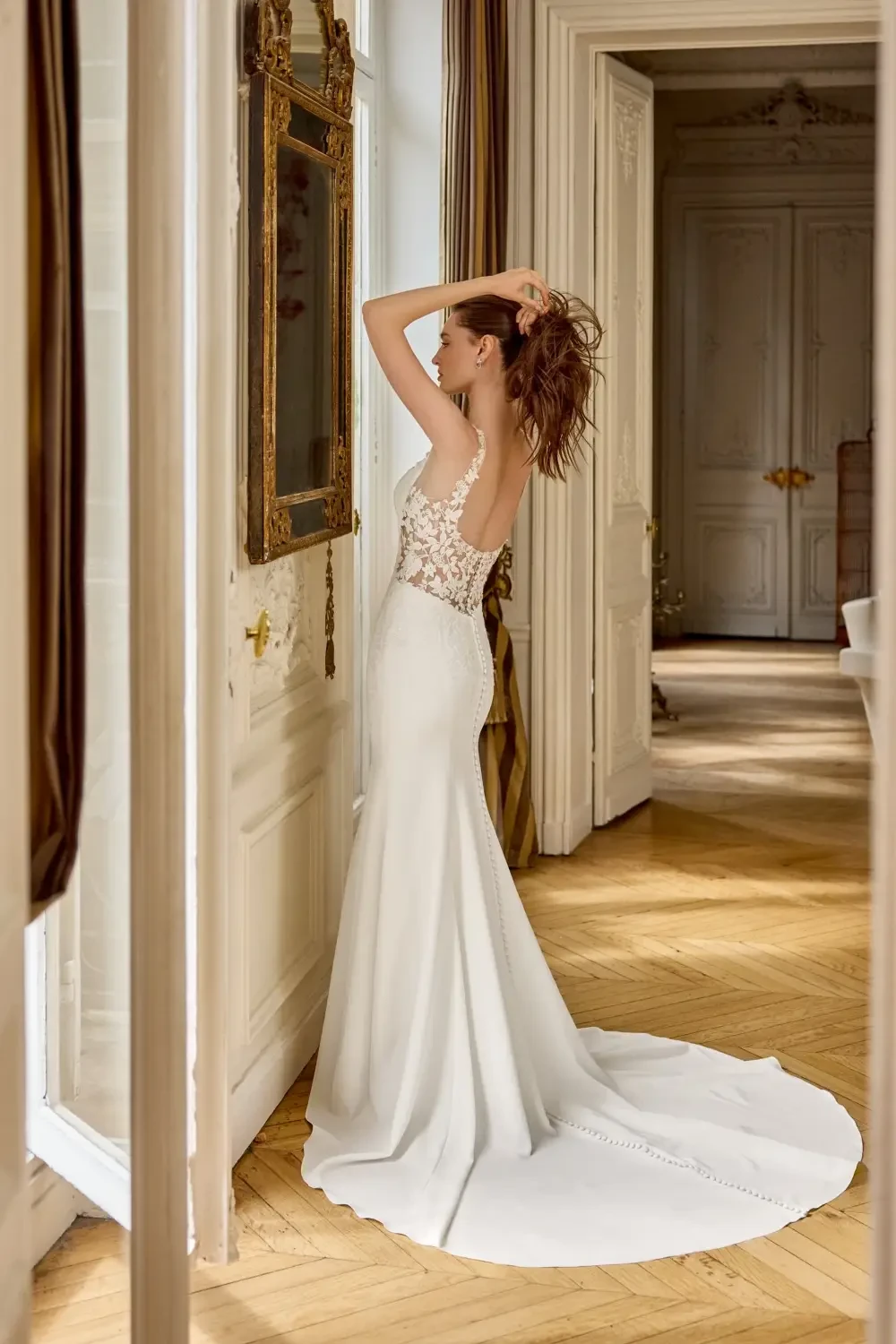 A woman wearing a fitted white wedding dress with lace detailing, standing next to a decorative iron railing.