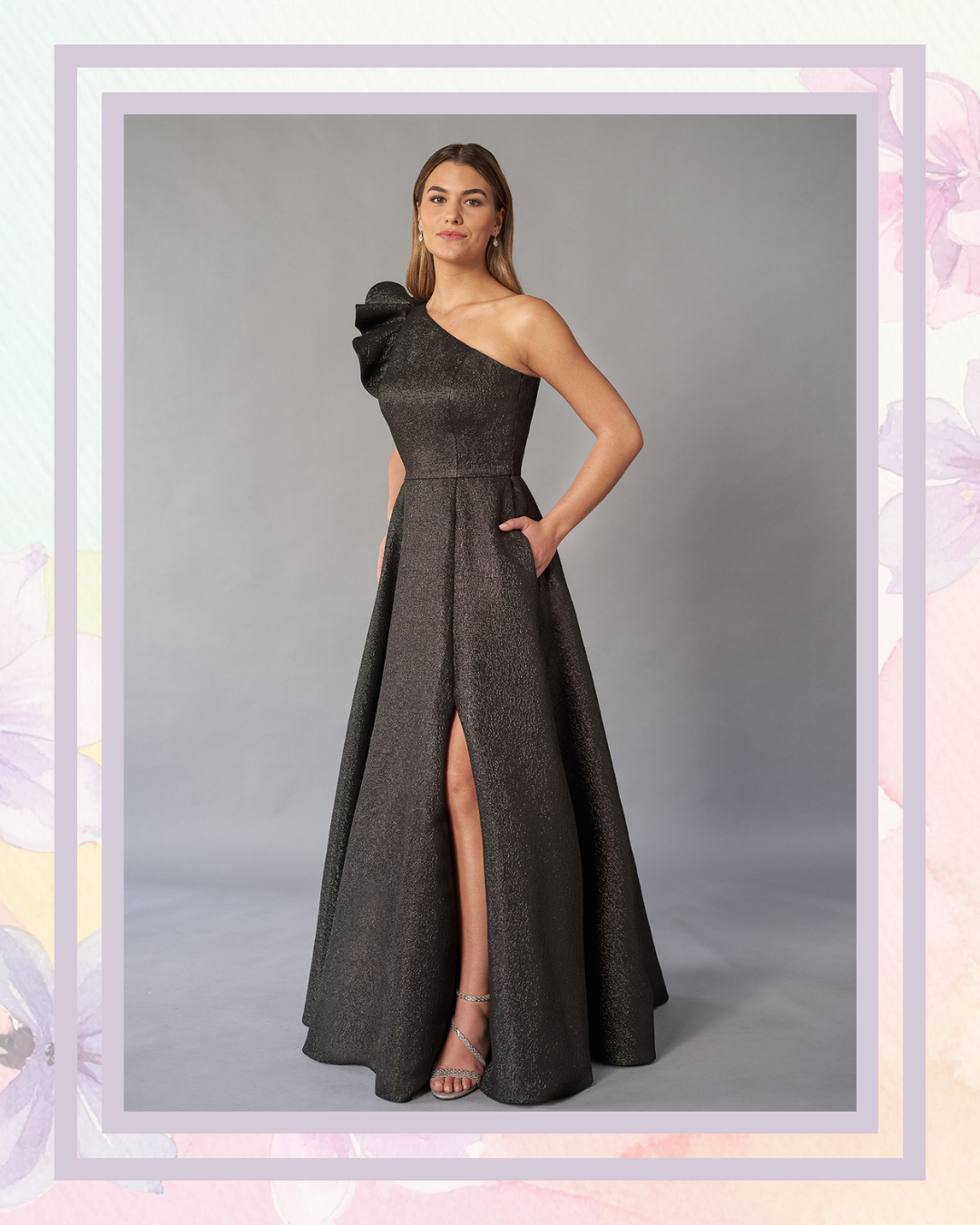 A woman in a one-shoulder black gown with a side slit and pockets, posing against a neutral backdrop.
