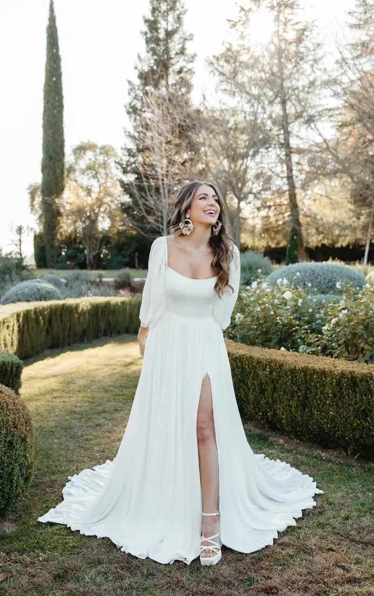 model is wearing a square neckline long sleeve a-line bridal gown with a slit