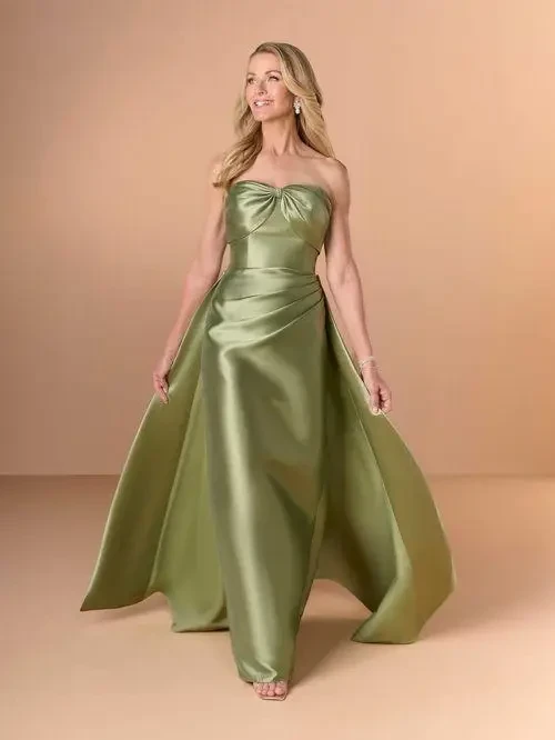 A woman in a strapless, satin green gown with a flowing train, smiling and posing against a neutral background.