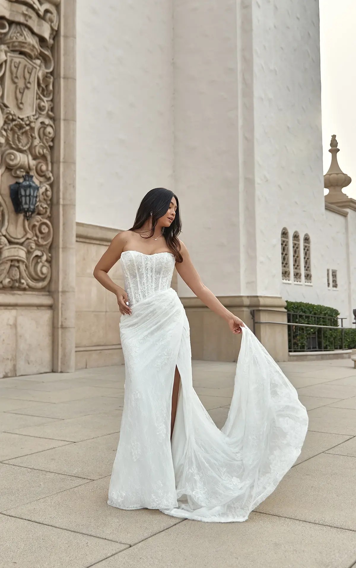 Model is wearing a strapless column wedding dress with exposed boning on the bodice