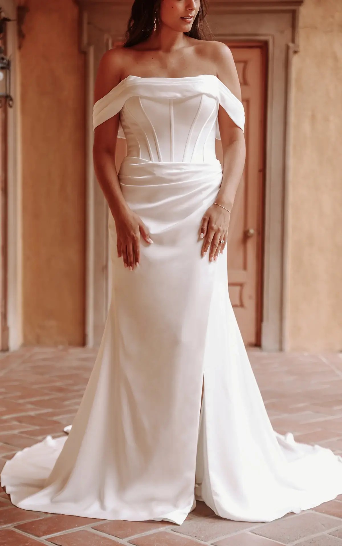 Model is wearing a fit and flare off the shoulder wedding dress with exposed boning on the bodice