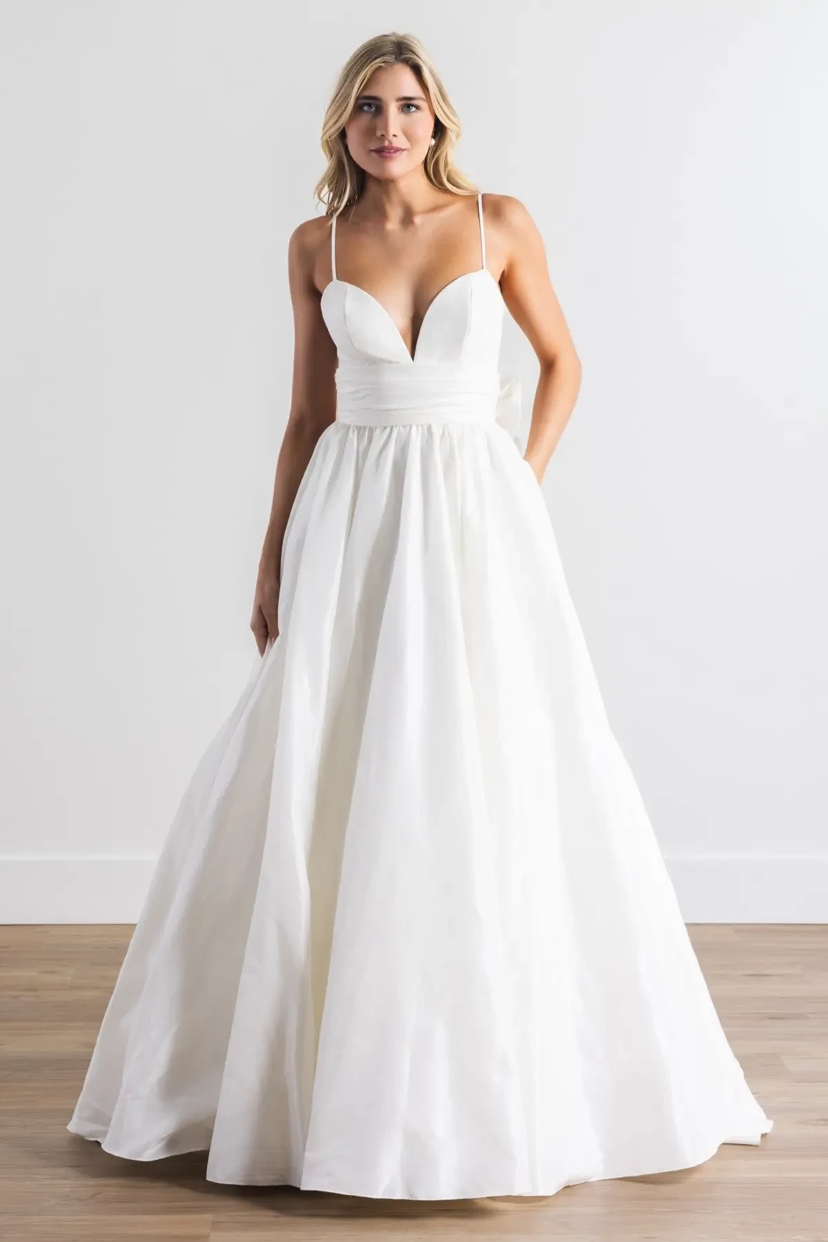 A woman in a sleeveless white gown with a plunging neckline and a full skirt, standing against a plain background.