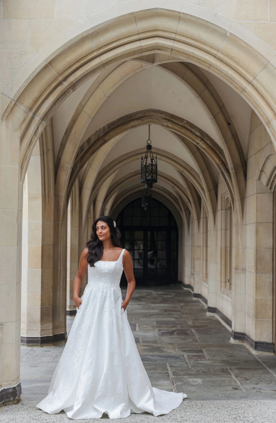 Model is wearing a sleeveless a-line wedding gown with a square neckline and long train