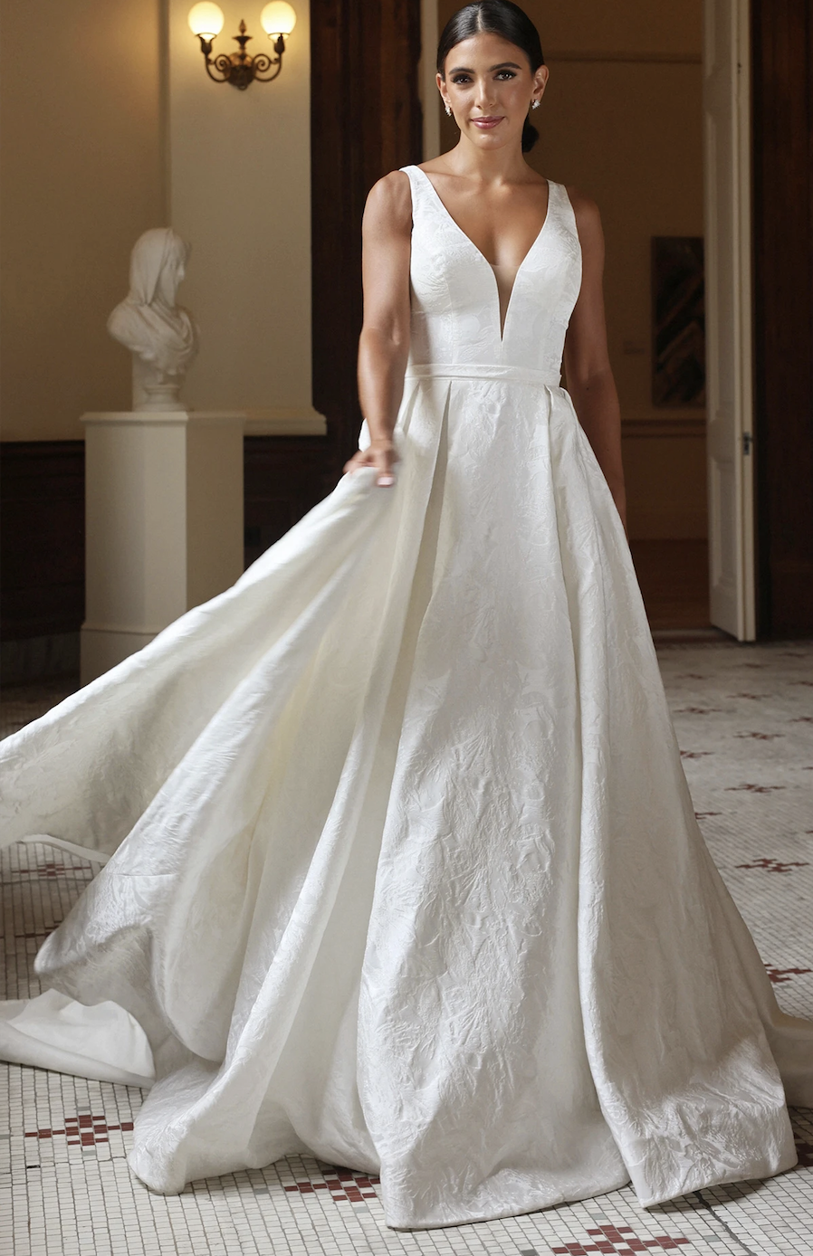 Model is wearing a sleeveless ball gown wedding dress with a plunging neckline and fitted bodice