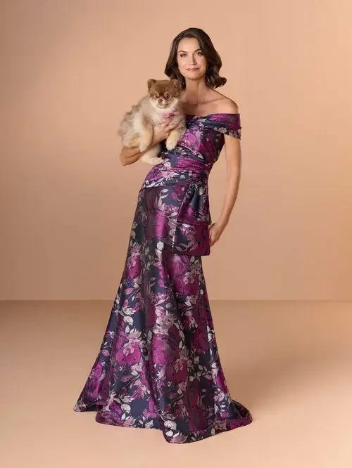 A woman in an off-the-shoulder floral gown holding a small dog, posing against a light background.
