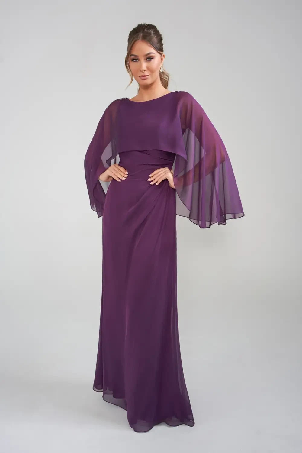 A model wearing a long, flowing purple dress with sheer, cape-like sleeves.