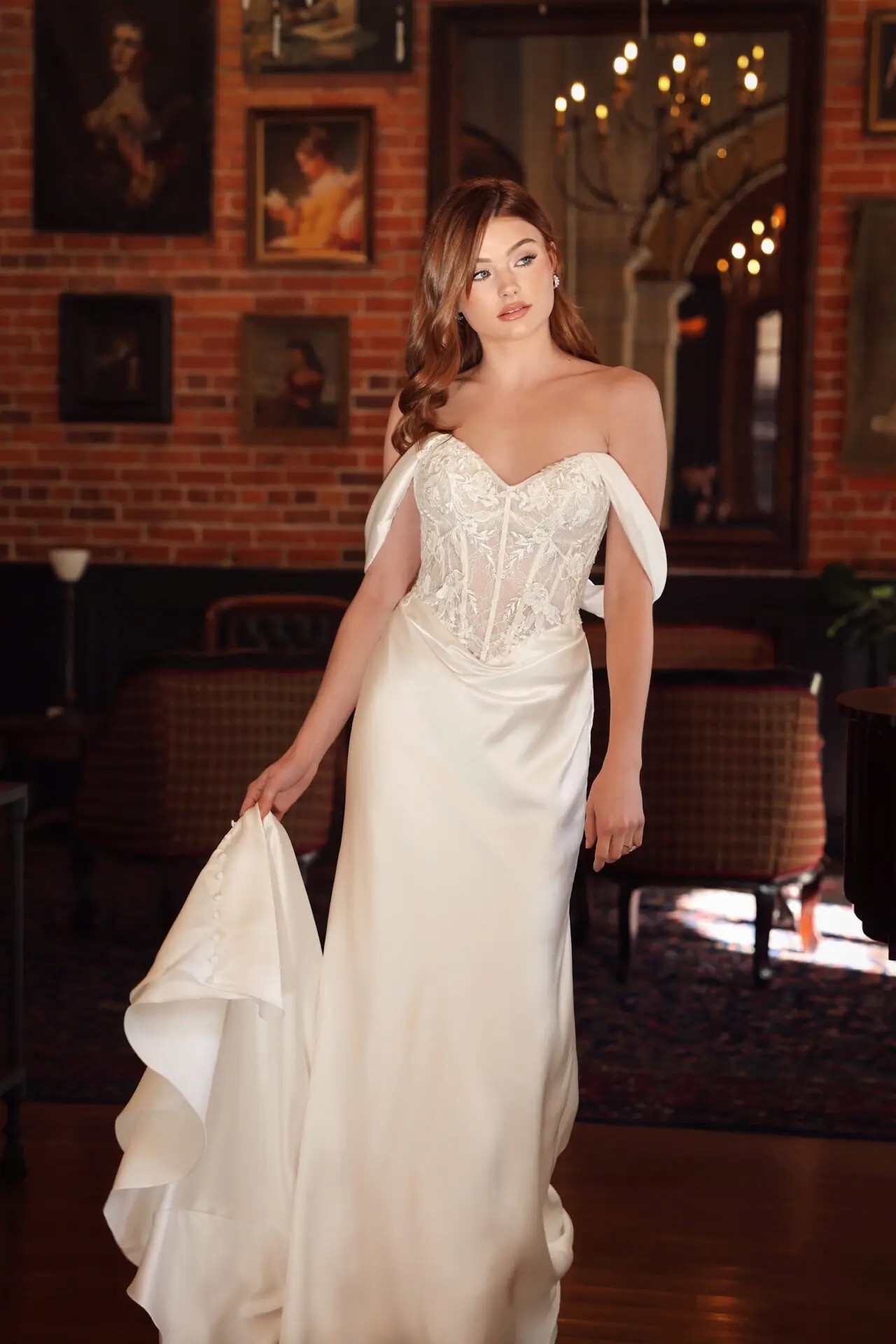 Model is wearing an off the shoulder column wedding dress with a dropped waist and lace bodice