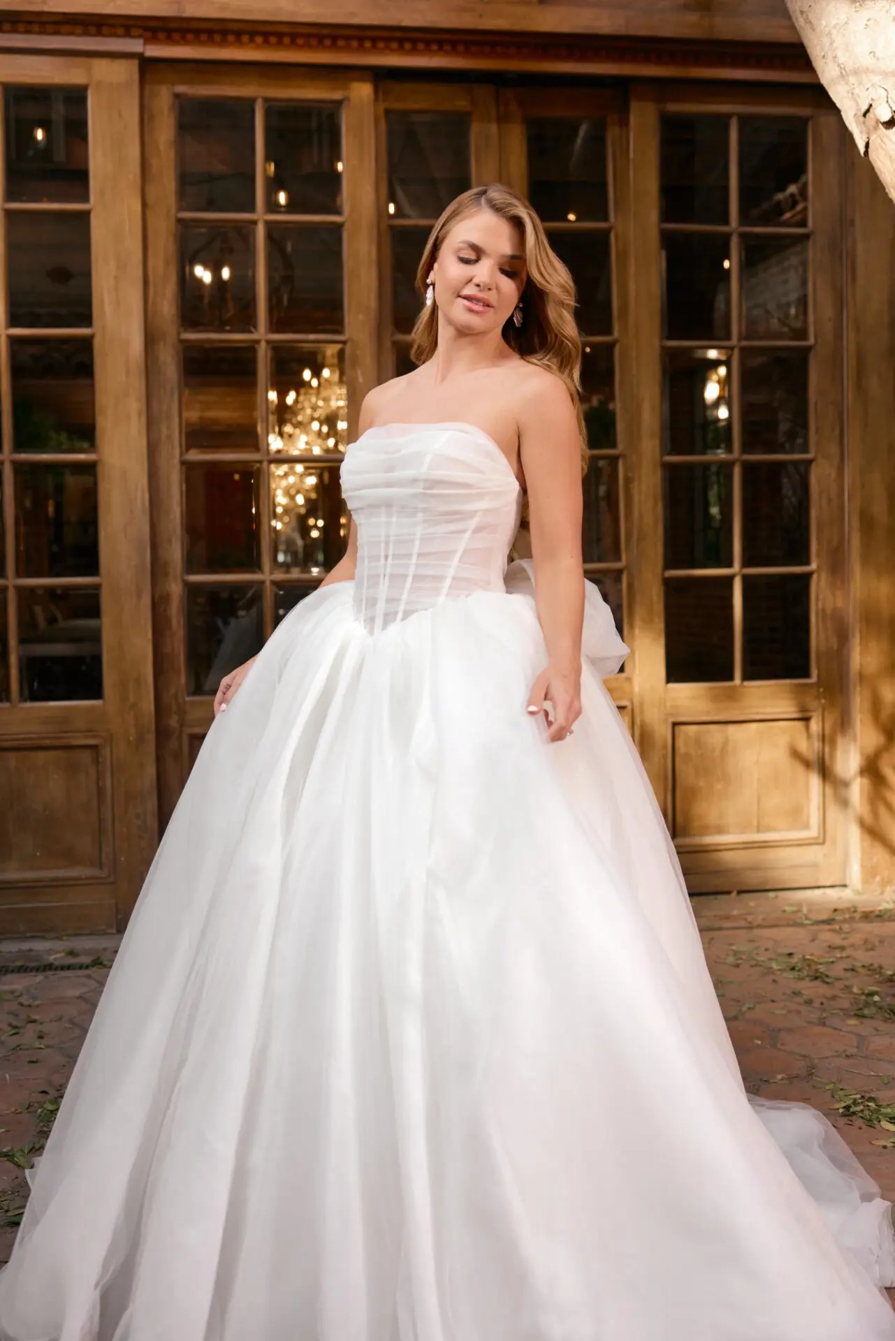 Model is wearing a strapless ball gown with a dropped waist and ruching on the bodice and drop waist