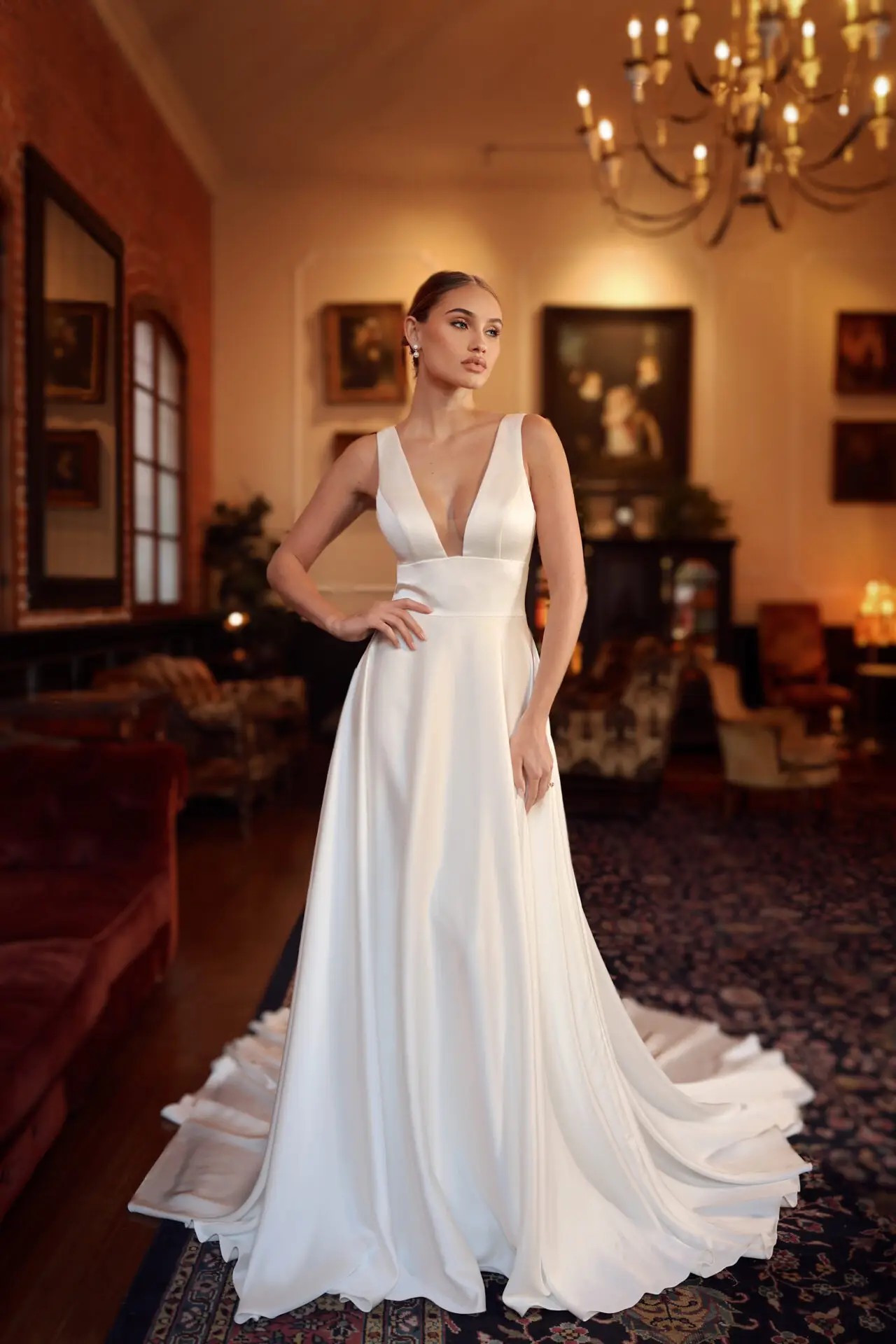 Model is wearing a sleeveless a-line wedding gown with a plunging neckline and satin finish with a long train